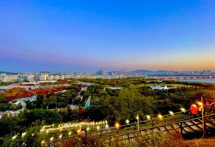 夕暮れから夜へと移ろう空と、遠くにきらめき始めたソウルの街明かりを、ハヌル公園の静かな丘の上から眺める。