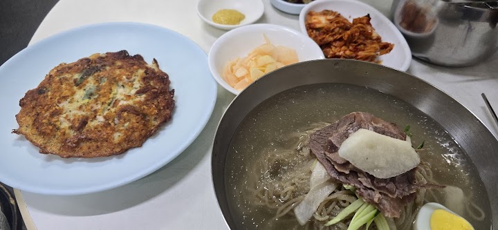 ソウルの麻浦にある乙密台で、冷たい金属の器に入った平壌冷麺と、香ばしく焼かれた緑豆チヂミのセットを楽しむランチタイム。